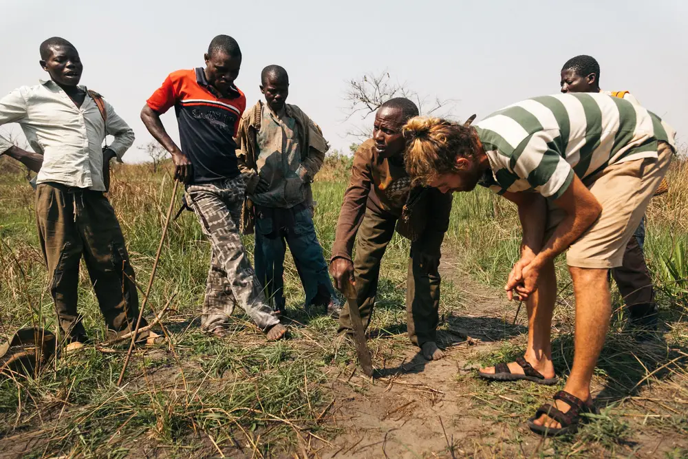 A fisherman draws in the dirt with a machete to outline the best route for tackling the next set of rapids.