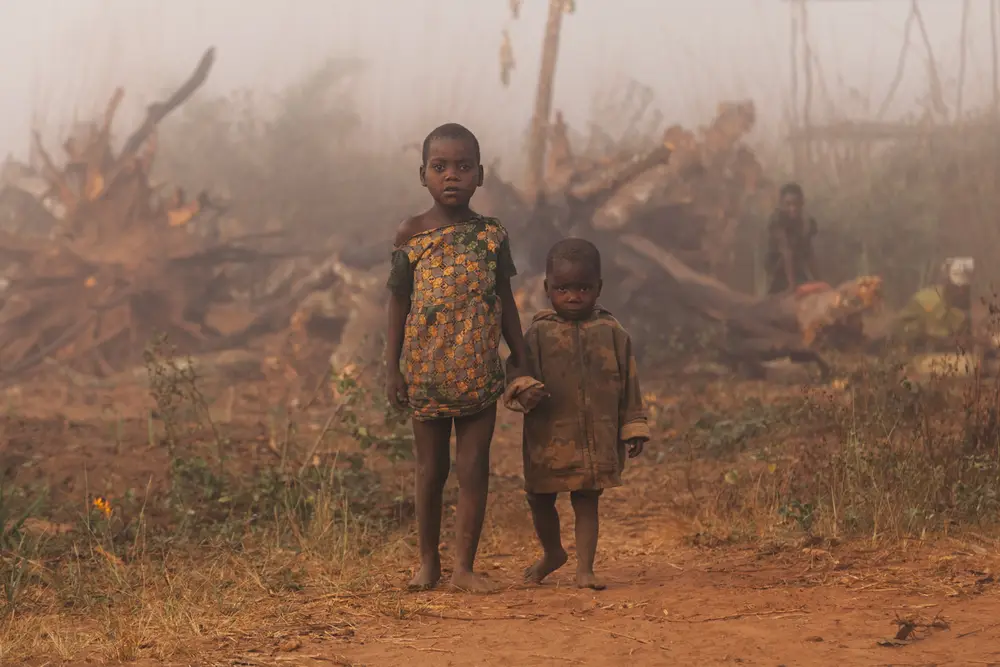 A young boy is lead by his older sister back to their home on the roadside.