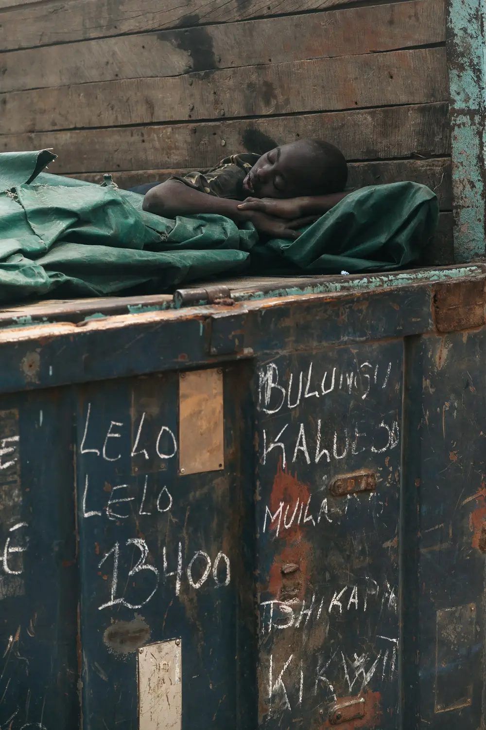 A boy takes a rest in a recently unloaded truck. Names of towns on the trucks passage are marked on the back door.